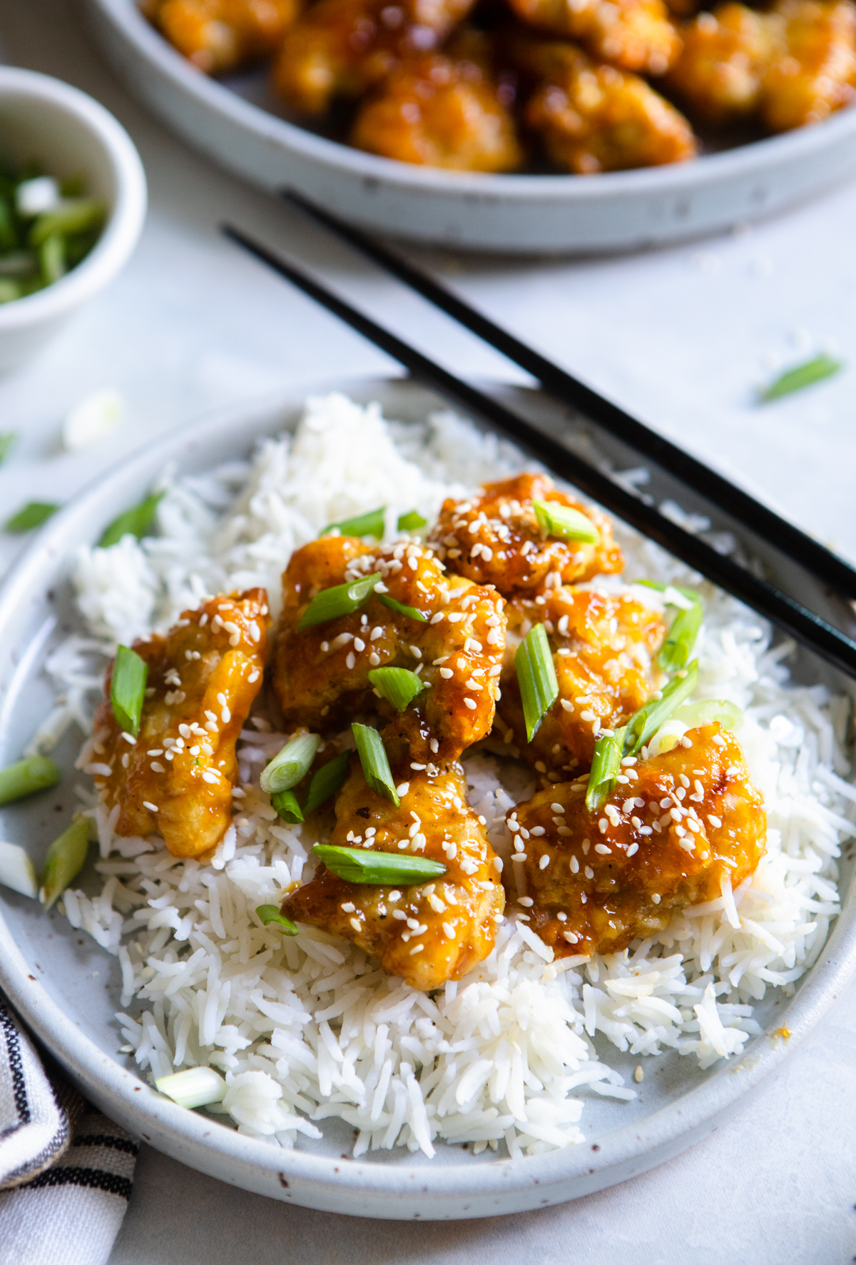 Air fryer orange chicken on a bed of rice on a round plate with chopsticks