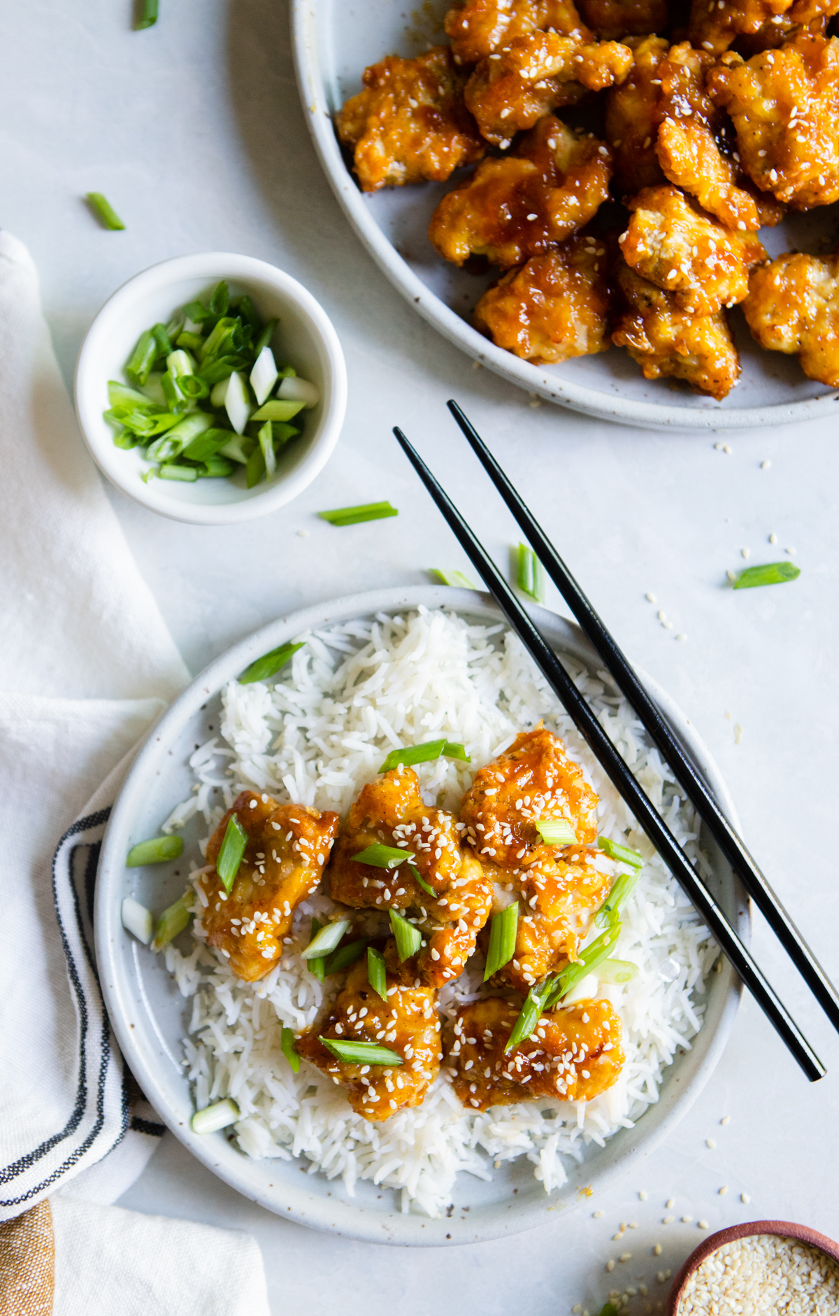 2 round plates filled with air fryer orange chicken topped with sesame seeds and scallions on a white board