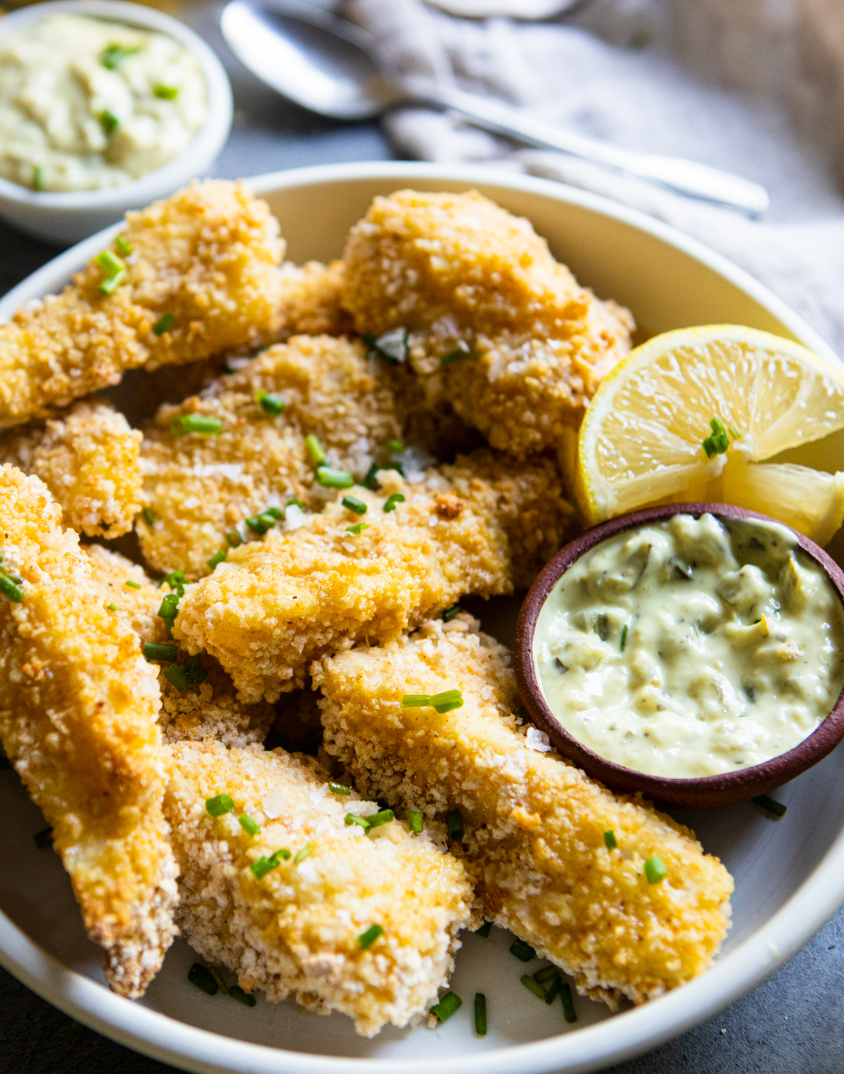 close up shot of fried fish sticks made in the air fryer next to a small bowl of tartar sauce and lemon wedges