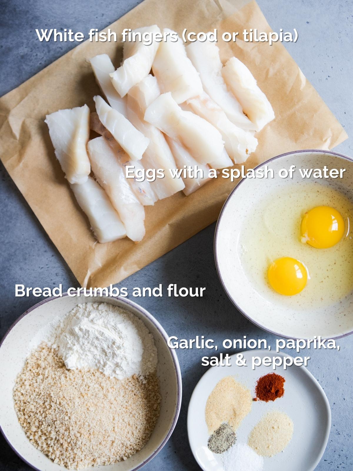 ingredients to make fish sticks including raw cod pieces, spices, flour, breadcrumbs and eggs, placed in little bowls