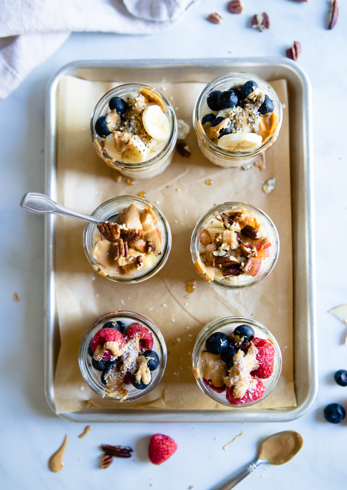 overhead shot of 8 ounce mason jars on a tray, filled with oats soaked in almond milk and topped with fruit and nuts