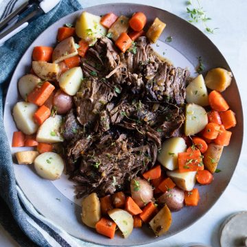 top round roast with gravy on a platter surrounded with potatoes and carrots and parsnips