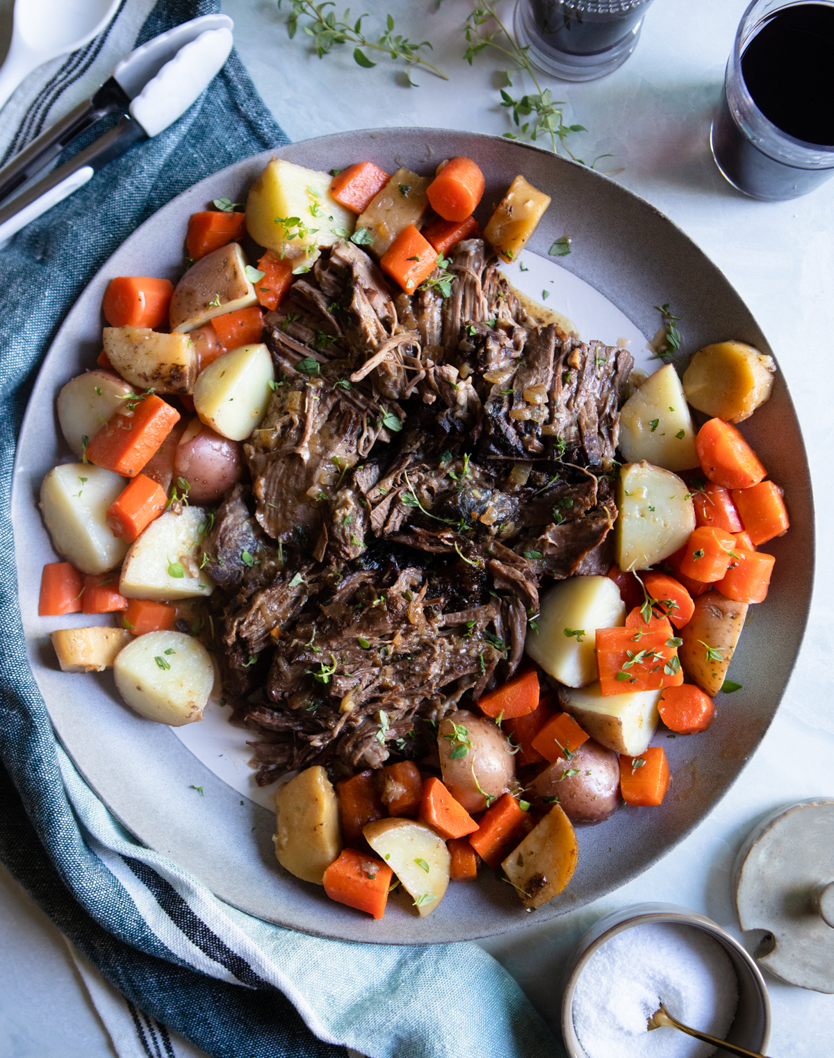 Top round roast cooked in a slow cooker on a gray platter surrounded by cooked root vegetables 