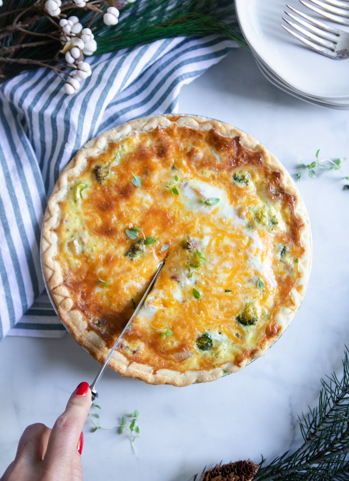 woman cutting into a broccoli and bacon Christmas quiche on a marble tapletop 