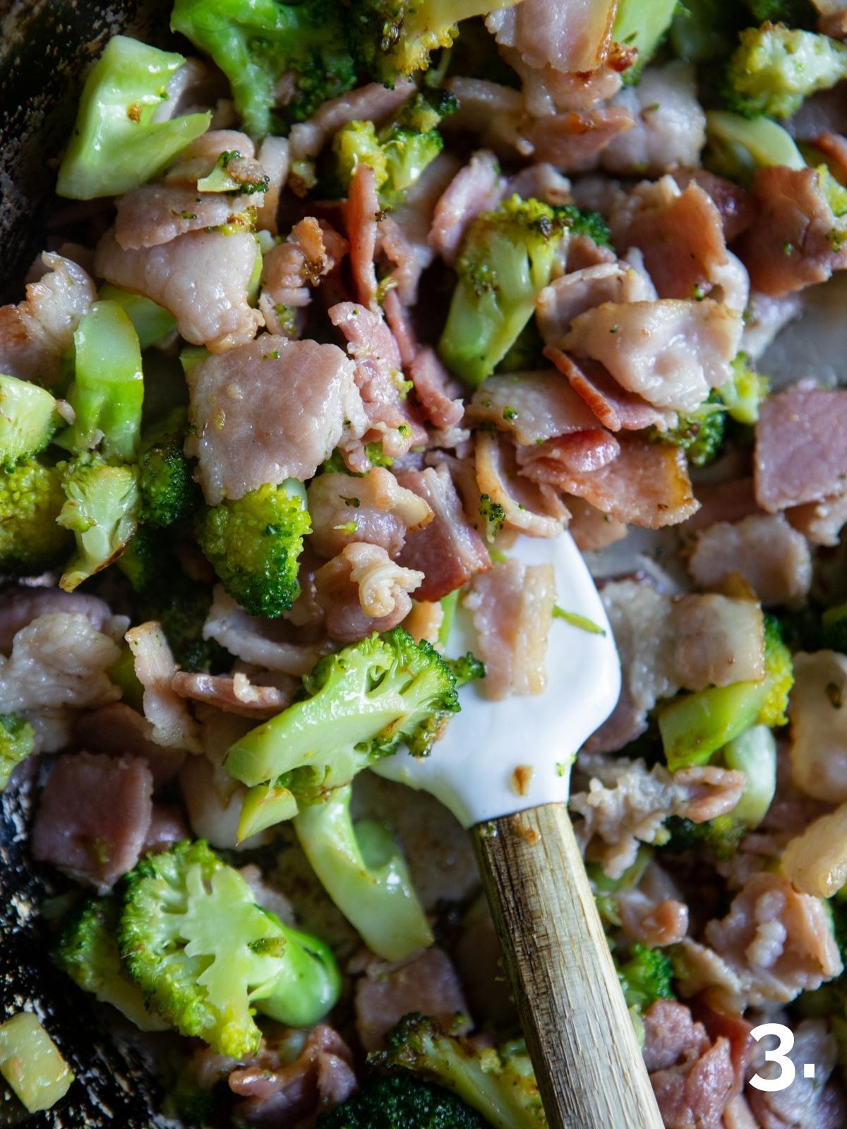 broccoli florets and bacon pieces being sautéed in a pan 
