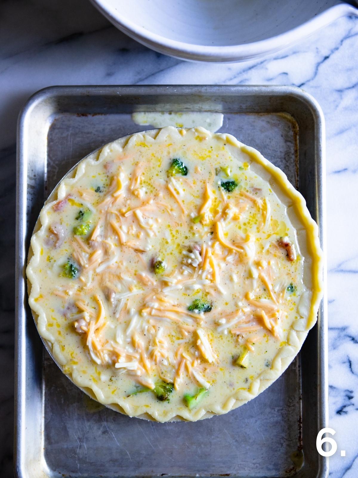 raw quiche in a pie pan placed on a baking sheet, ready to bake