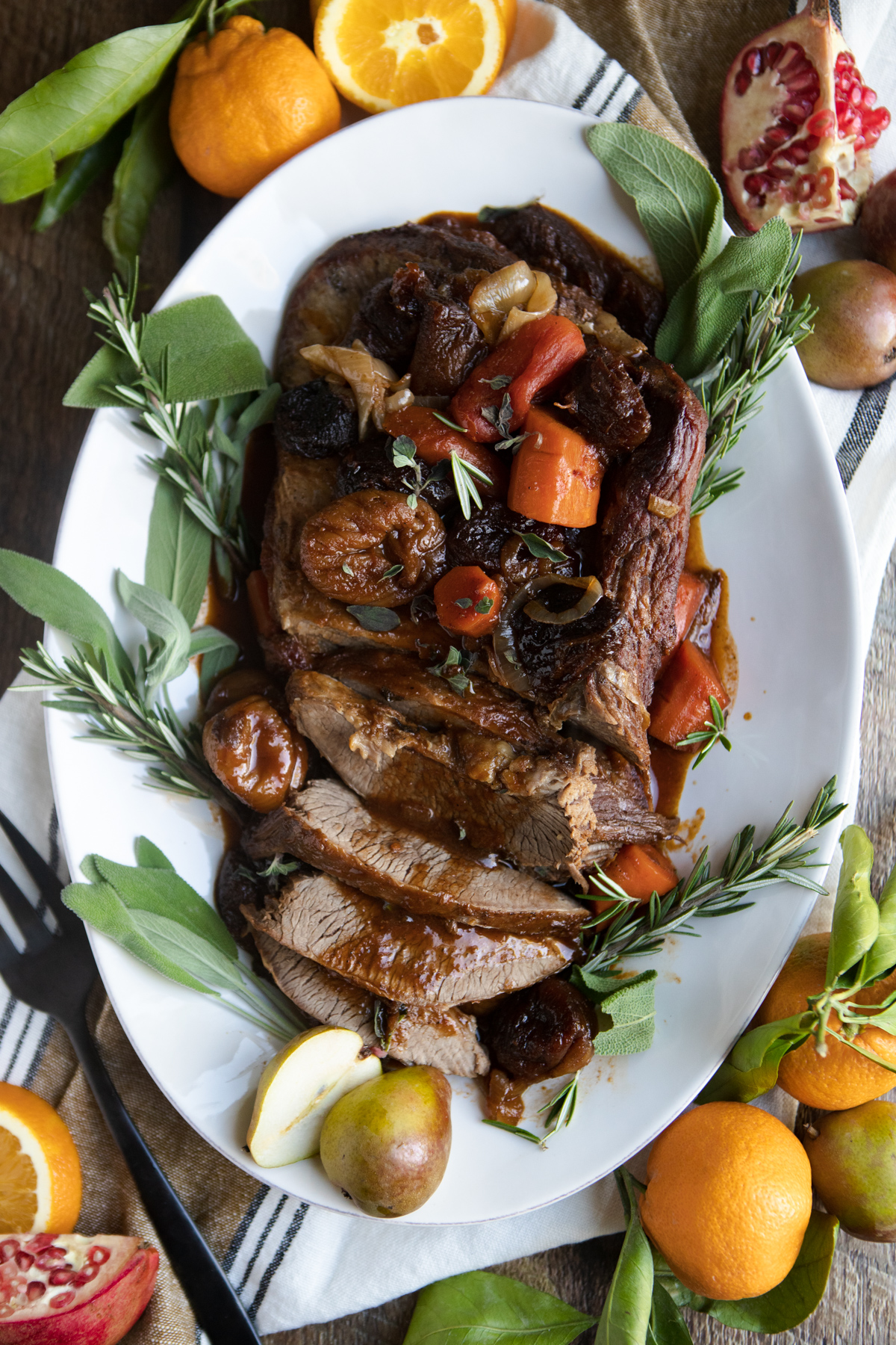 beef brisket on a white platter with dried fruit, tomatoes and carrots spooned on top