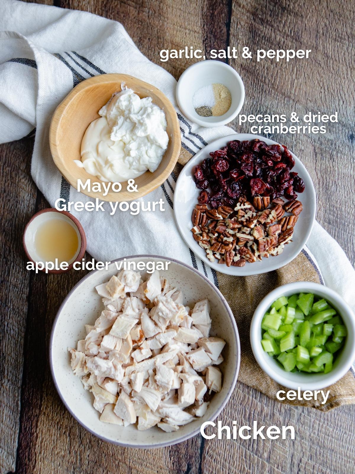 little bowls filled with raw ingredients to make chicken salad, on a wooden board