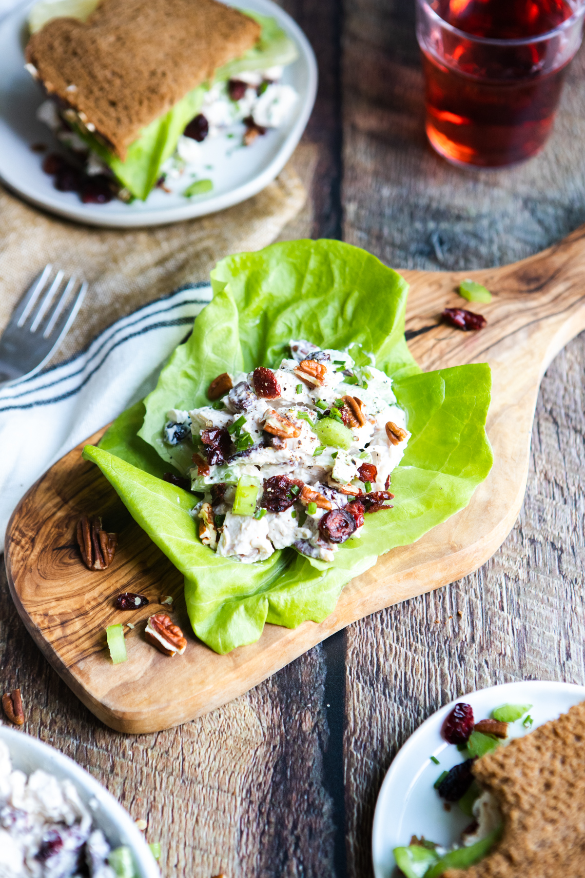 wooden board with a cranberry pecan chicken salad recipe lettuce wrap on top next to a plate with a sandwich on it 