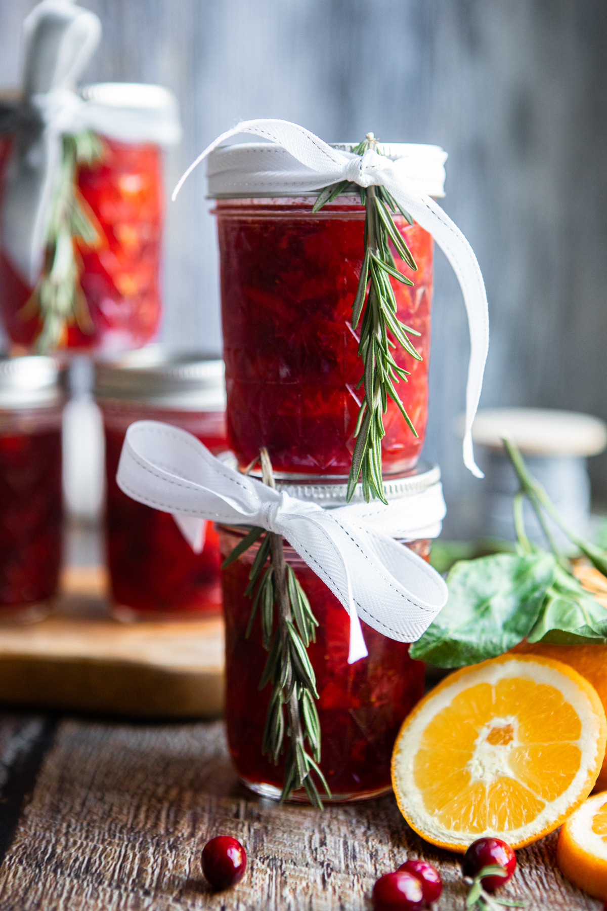 small mason jars filled with homemade cranberry strawberry rosemary jam tied with ribbon