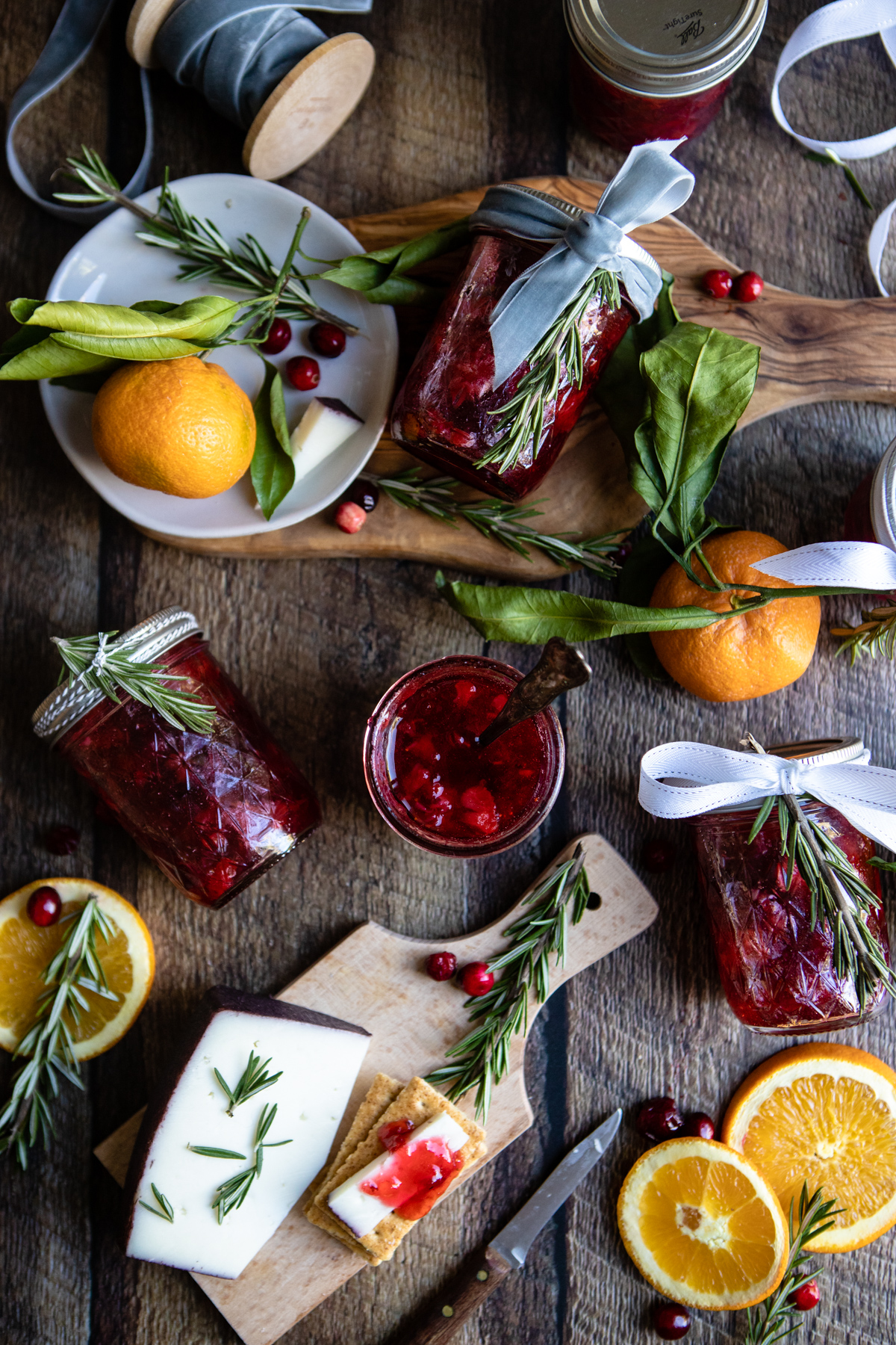 Christmas spread on a wooden board, with crackers and cheese, Christmas jam, clementine oranges. rosemary sprigs and spools of ribbon