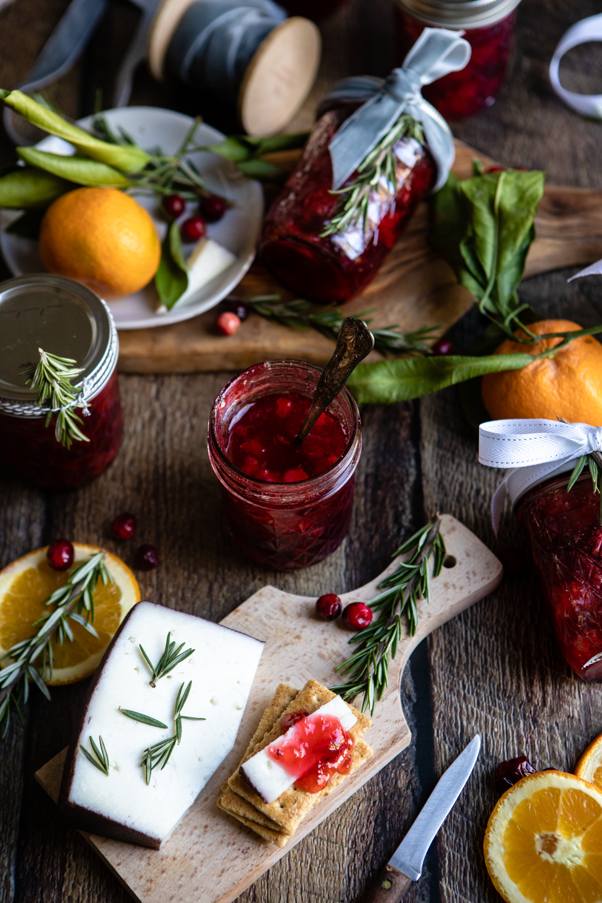 Cranberry rosemary Christmas jam jars on a wooden background, surrounded by oranges and cranberries