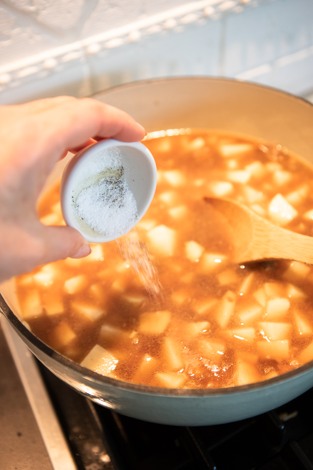 Dutch oven filled with soup with salt and pepper being poured in to flavor 