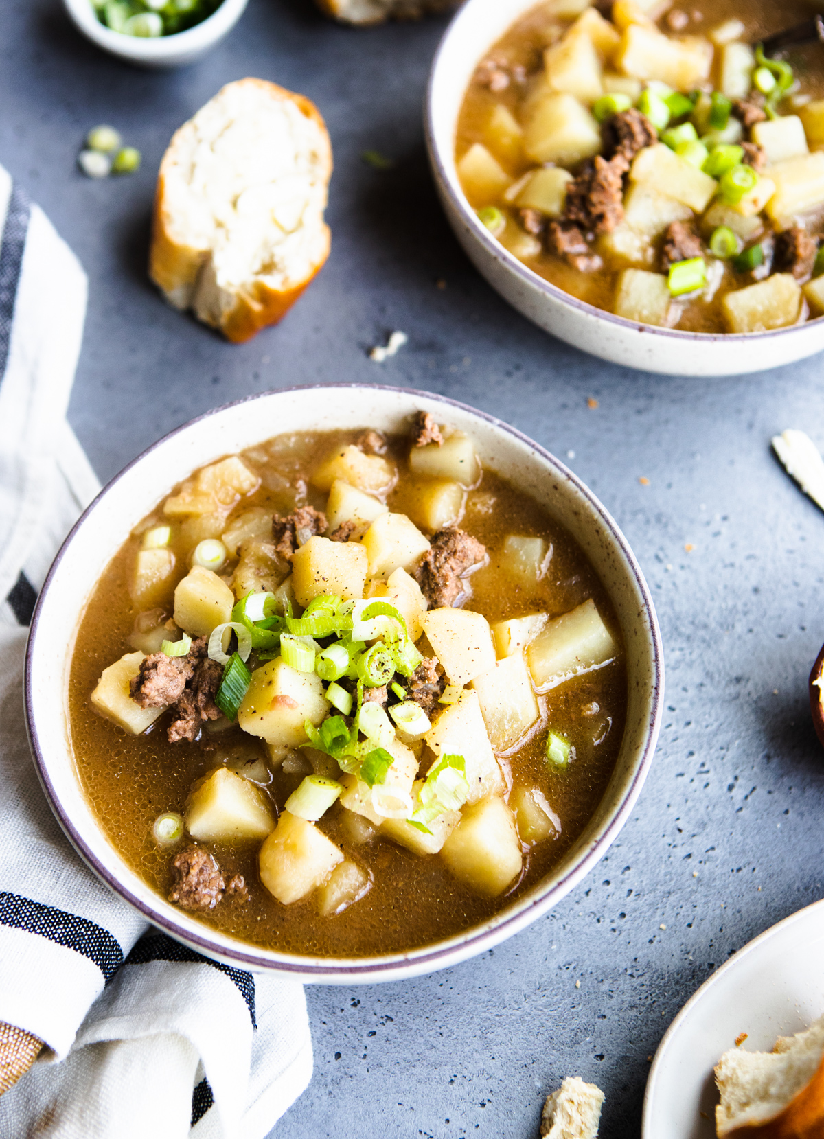 2 white bowls filled with hamburger potato soup and garnished with green onions on a gray background 