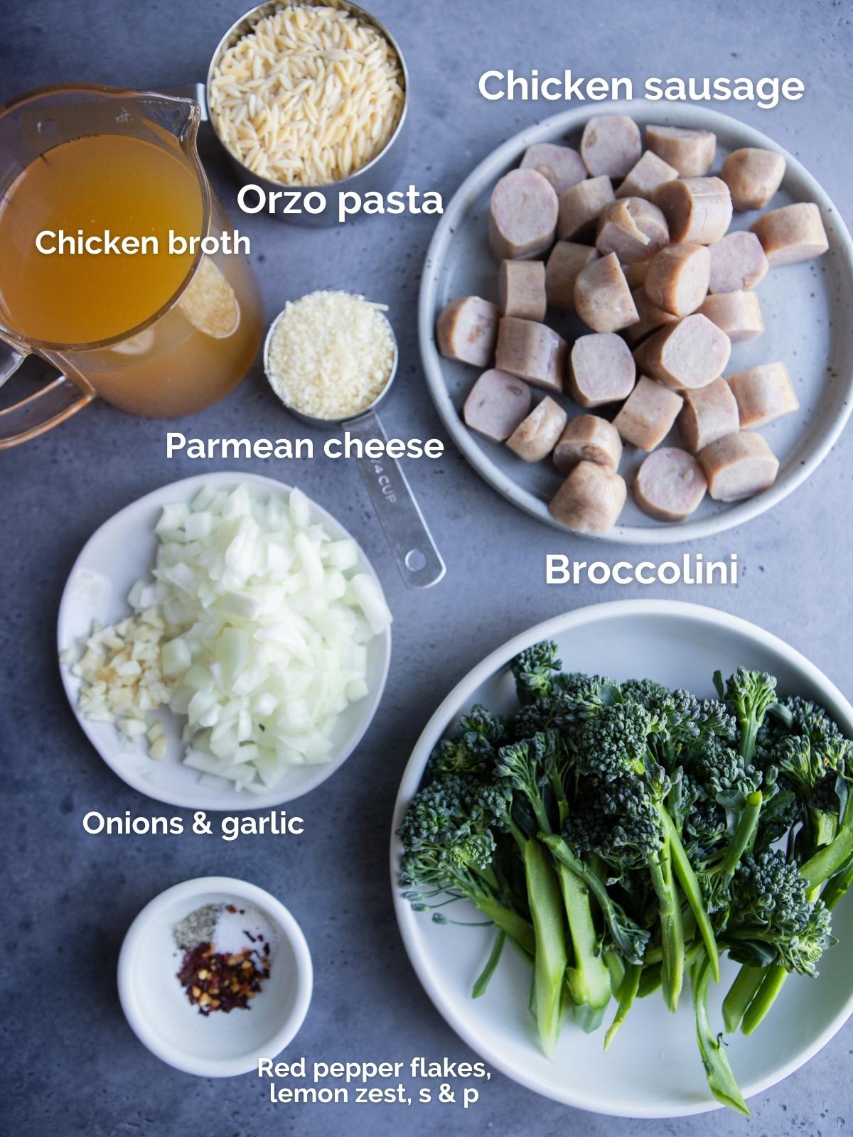 raw ingredients to make chicken sausage and orzo pasta on white plates on a gray board