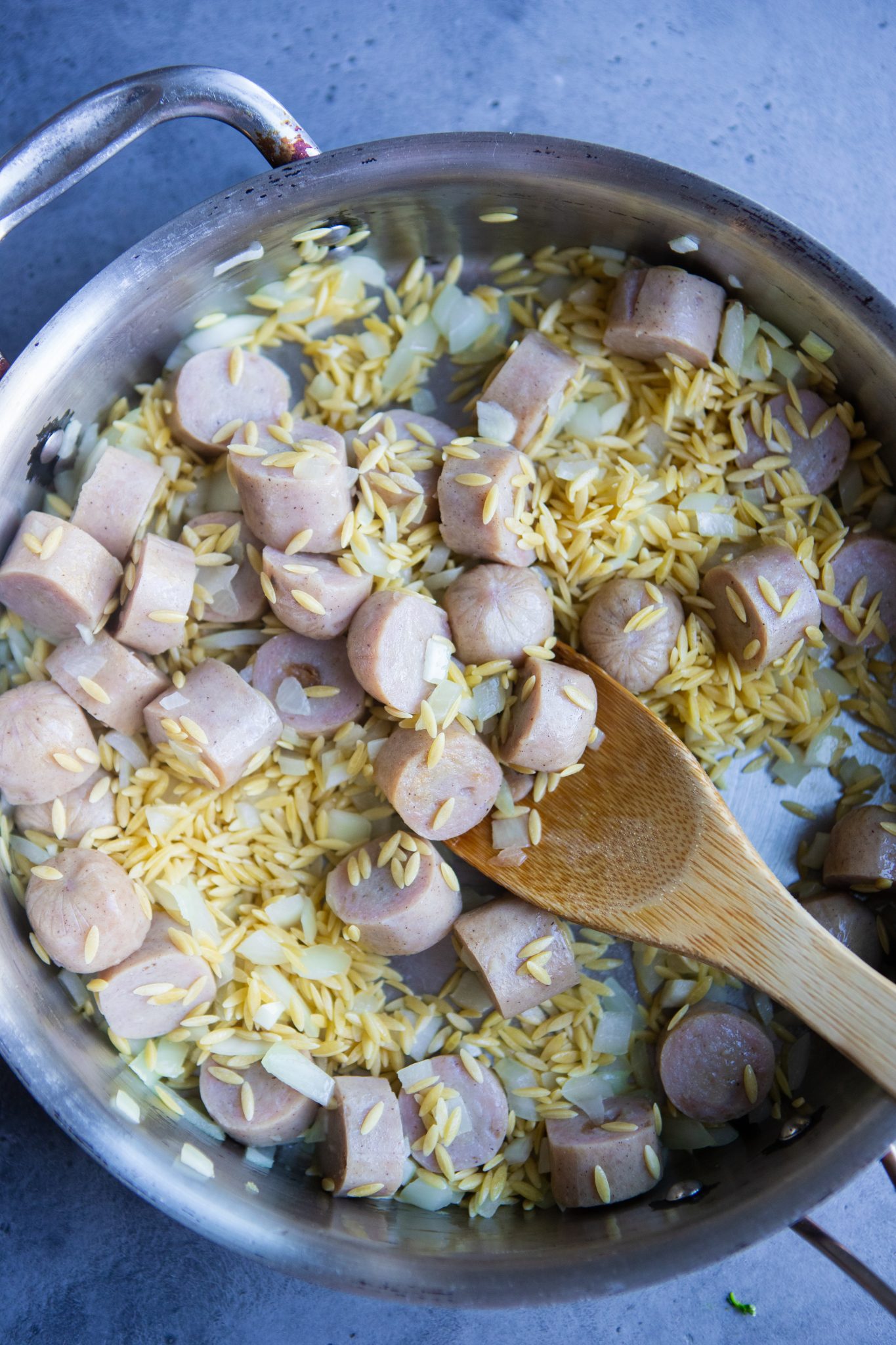 orzo diced onions and sliced sausage being sautéed in a large skillet