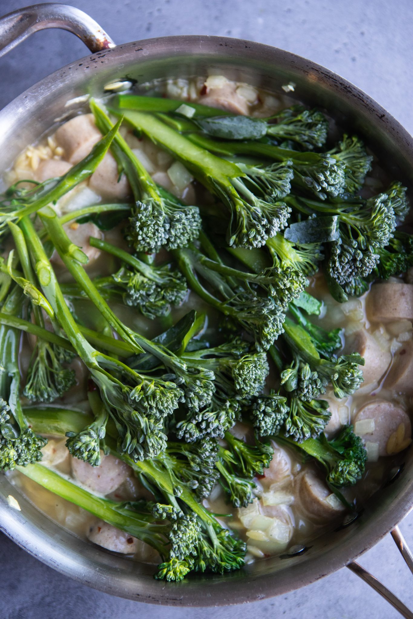 fresh broccolini in a skillet with orzo, chicken sausage and chicken broth