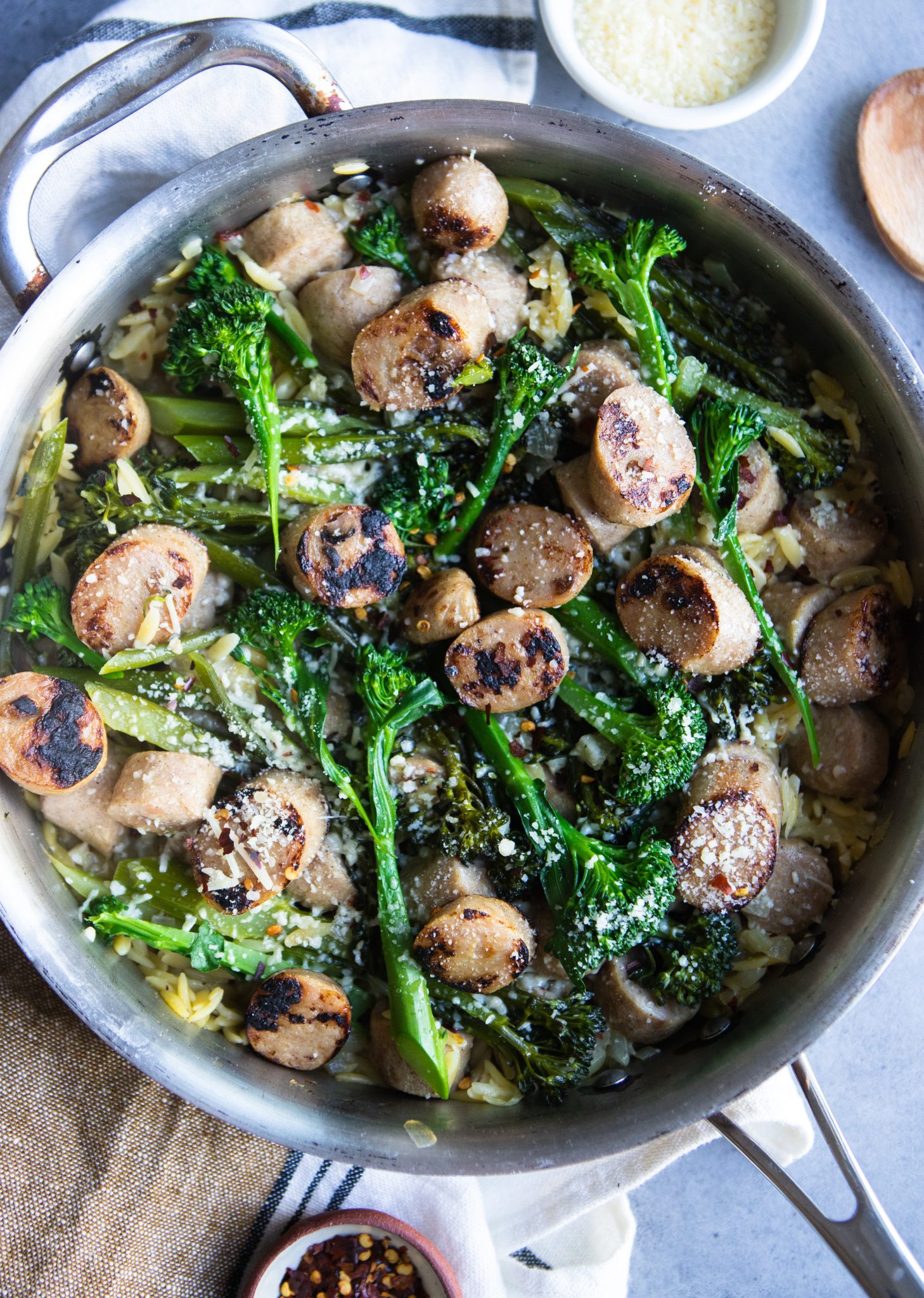 stainless skillet filled with broccolini, orzo pasta and sausages