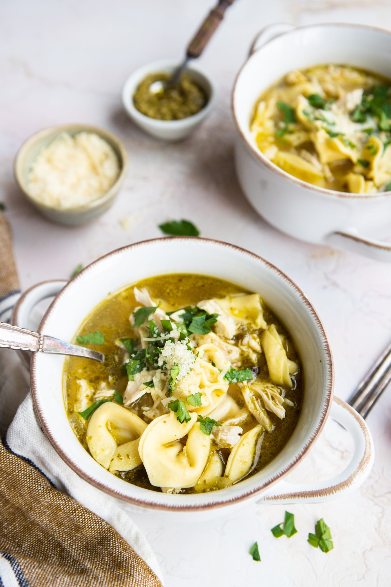 2 bowls filled with chicken tortellini soup and tiny bowls filled with pesto and parmesan cheese 