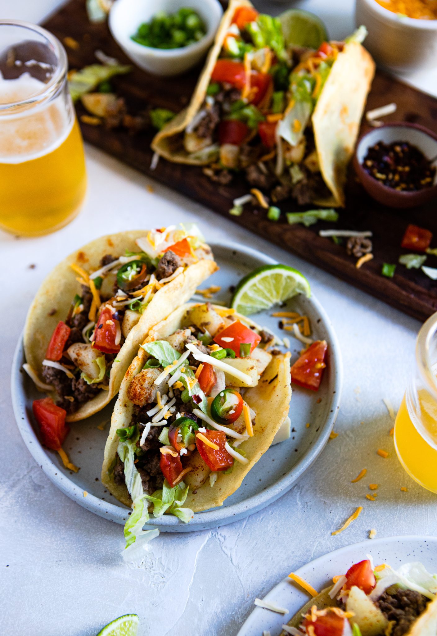 plate of fried taco shells filled with ground beef and potatoes topped with garnishes and sitting next to 2 glasses of beer