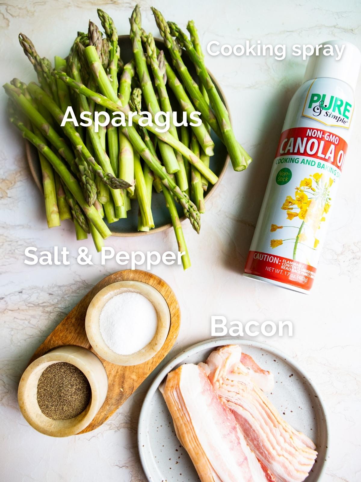 raw asparagus and bacon and cooking spray on a marble countertop 