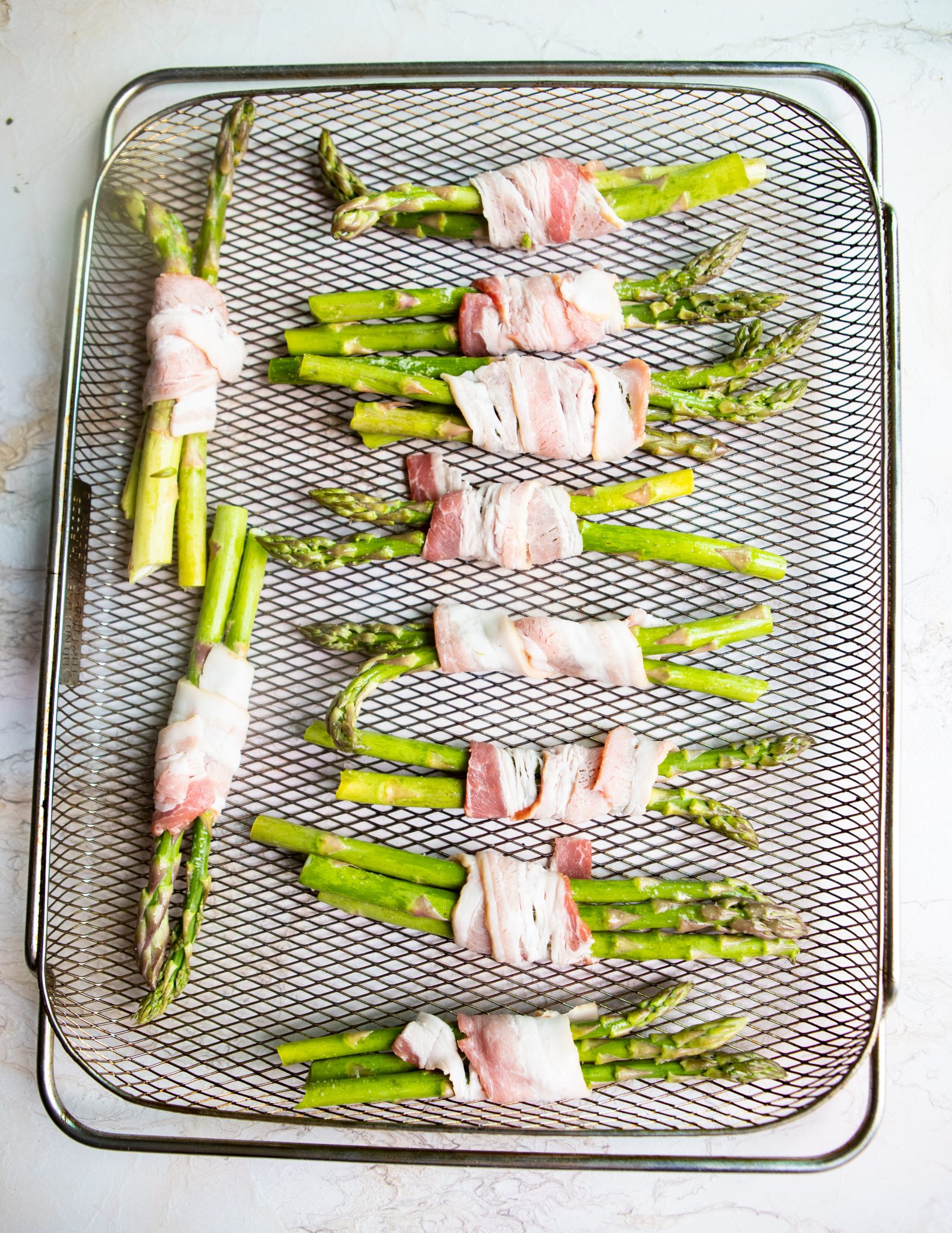 raw bacon wrapped asparagus air fryer cooked on a tray 