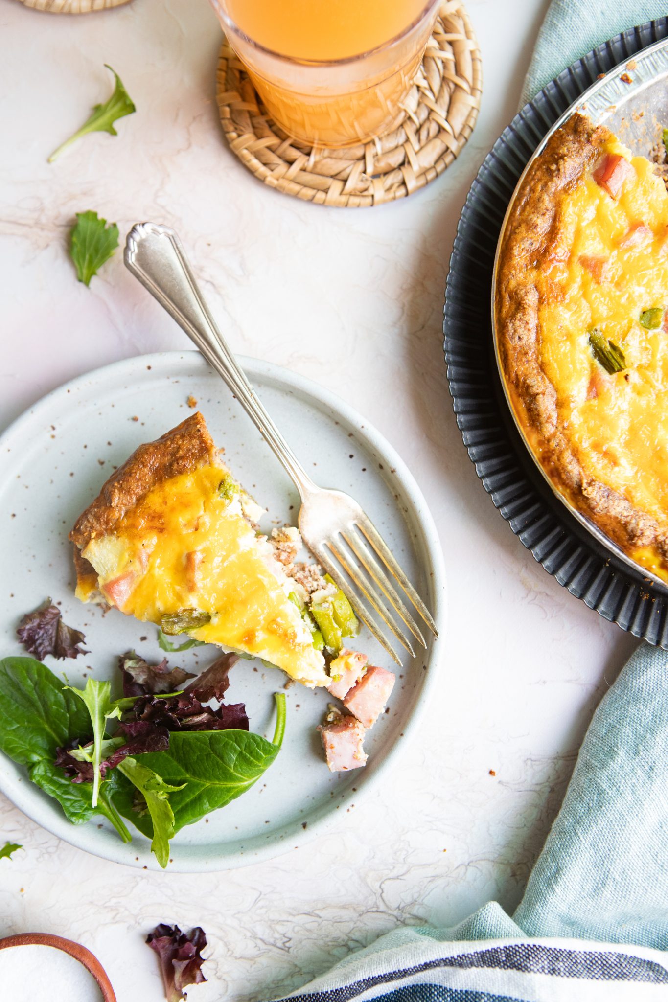 a piece of ham and asparagus quiche recipe on a gray plate next to a whole quiche