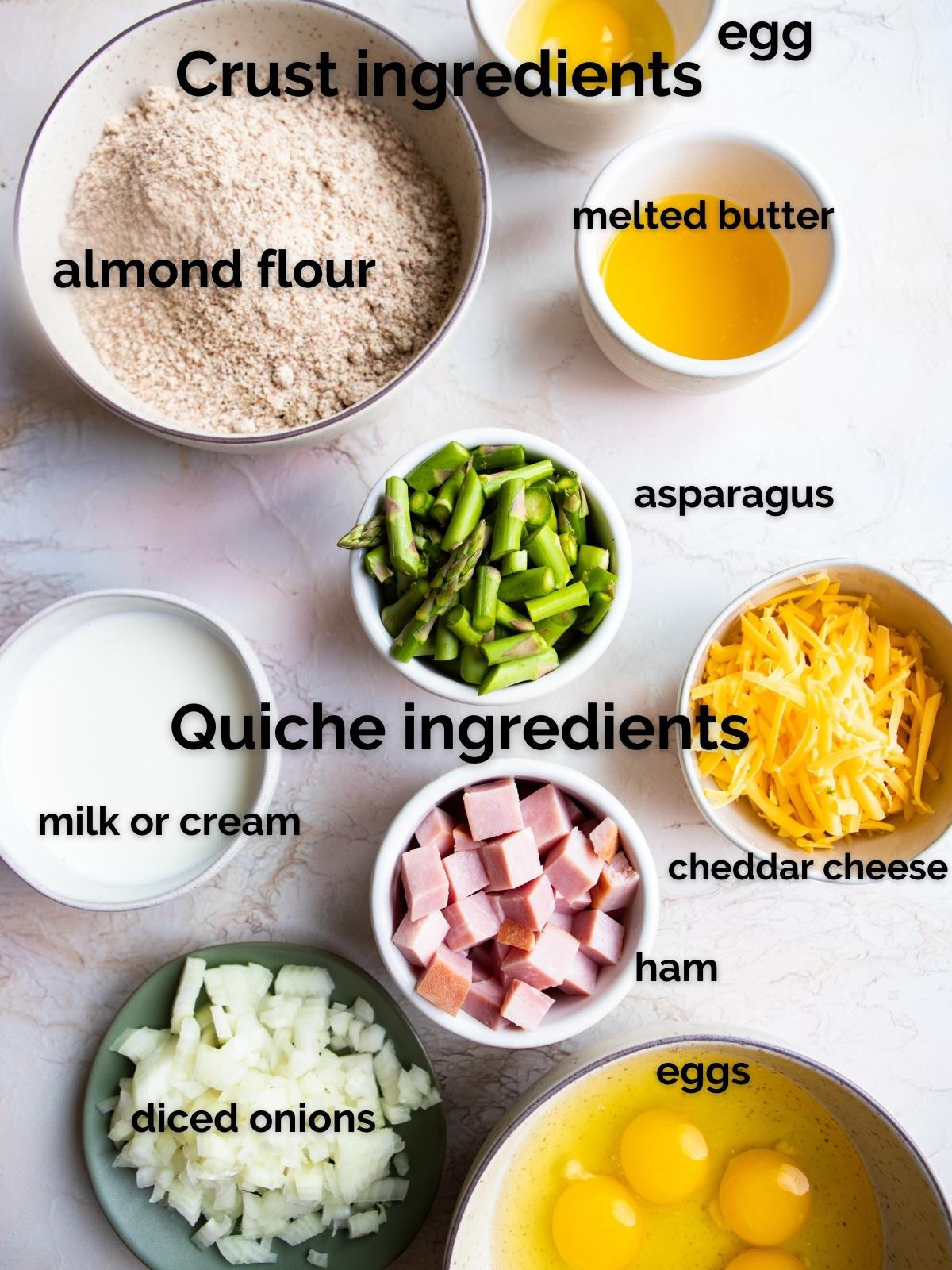 raw ingredients to make asparagus quiche in white bowls on a marble surface 