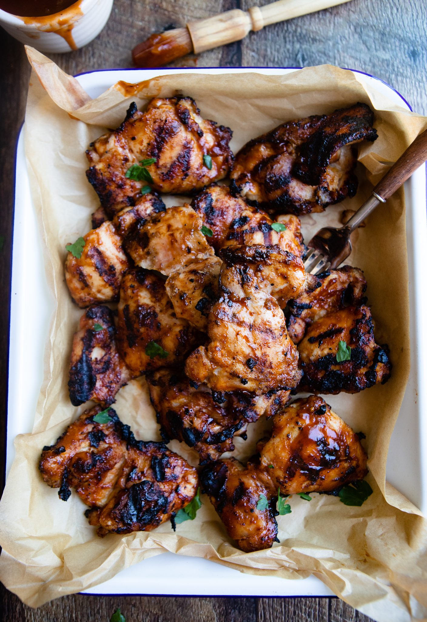 grilled boneless chicken thighs in a white metal baking sheet with barbecue sauce brushed on