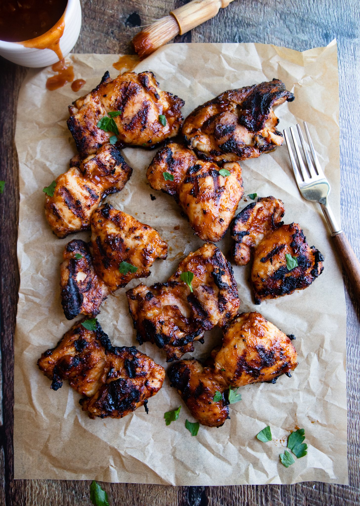 parchment paper with cooked chicken pieces on top rubbed with barbecue sauce