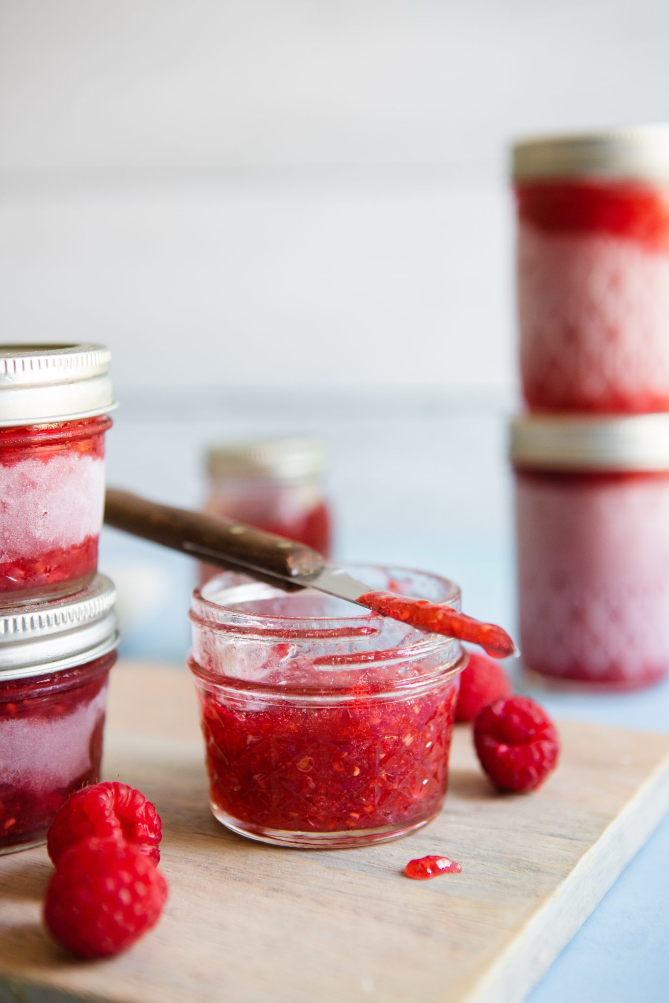 homemade raspberry freezer jam in small mason jars stacked up on a wood board 