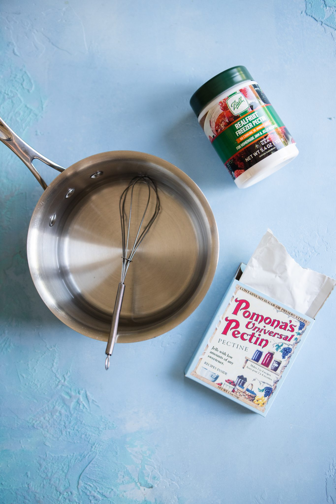 box of Pomona's Universal Pectin and Ball Real Fruit Freezer Pectin on a blue table next to a saucepan filled with water