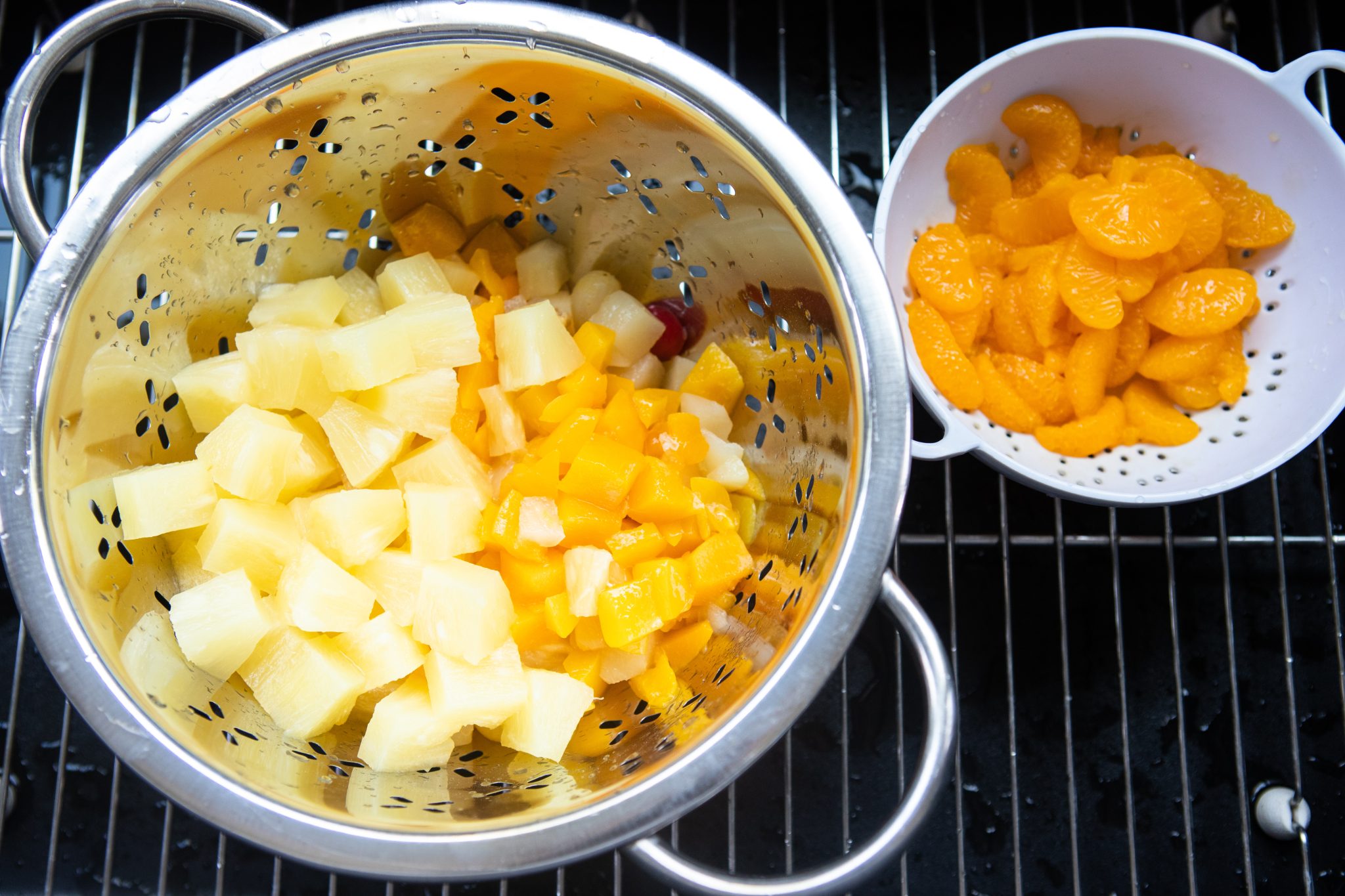 canned fruit salad and mandarin oranges in strainer over sink