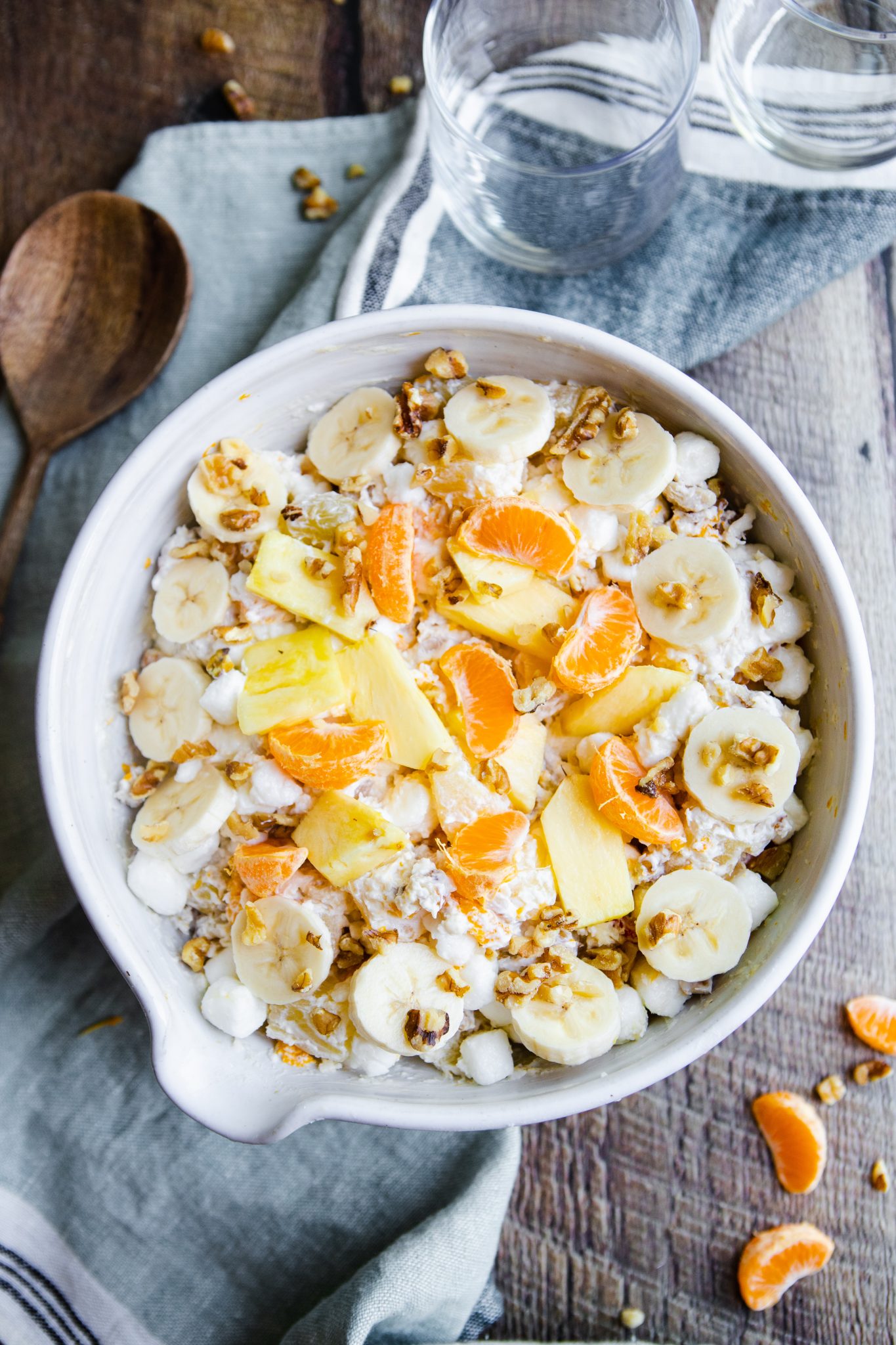 white ceramic bowl filled with ambrosia salad made with cool whip on a wood surface 