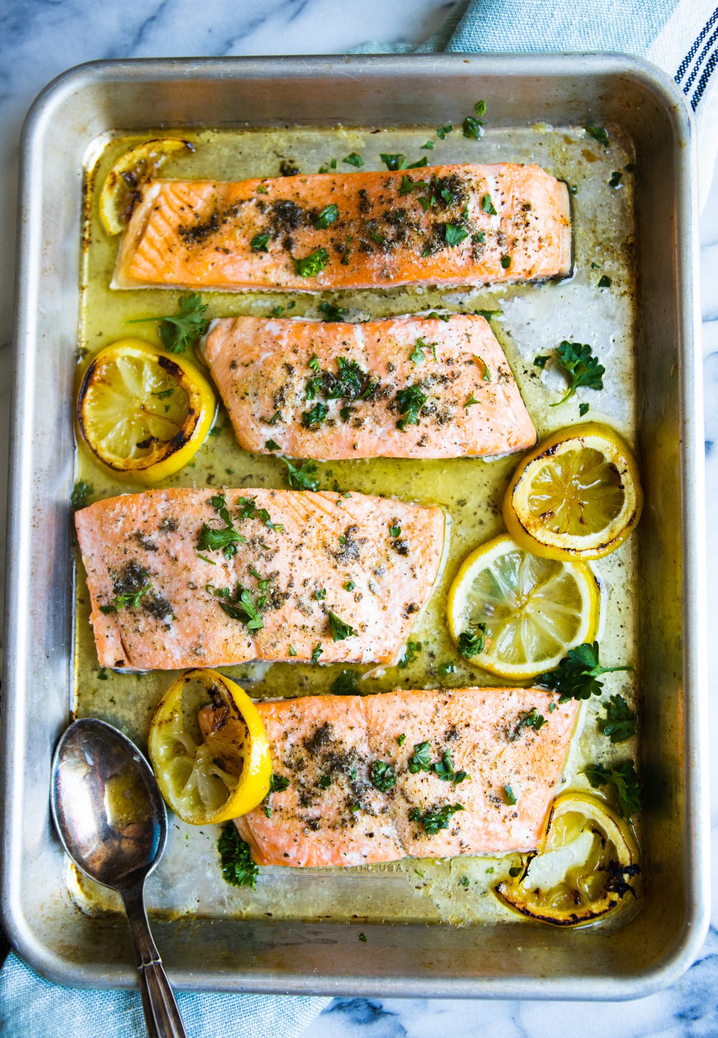 rimmed sheet pan filled with garlic butter salmon recipe and topped with fresh parsley 