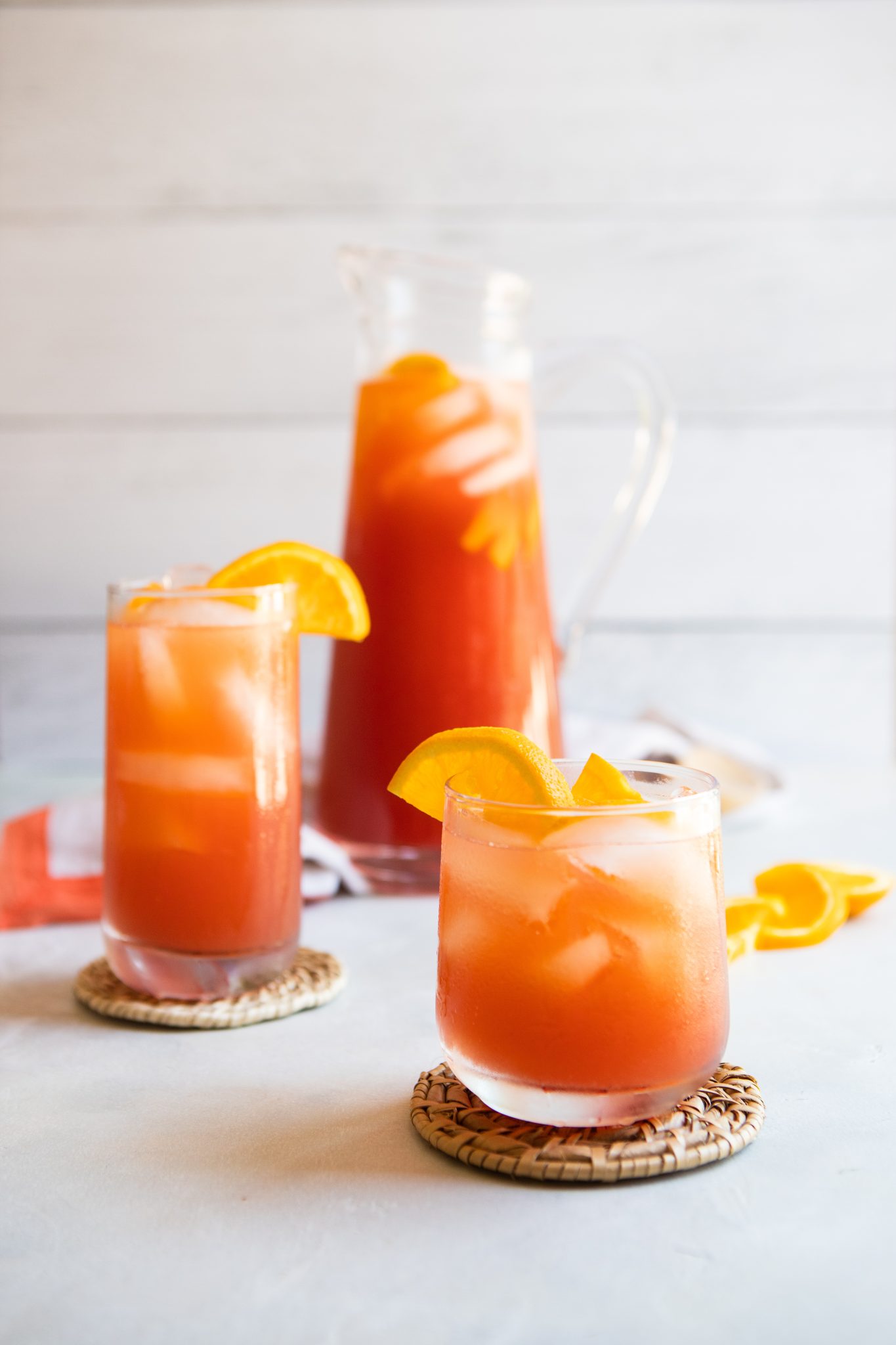 glass pitcher filled with fruit tea and garnished with oranges next to 2 glasses filled with iced tea
