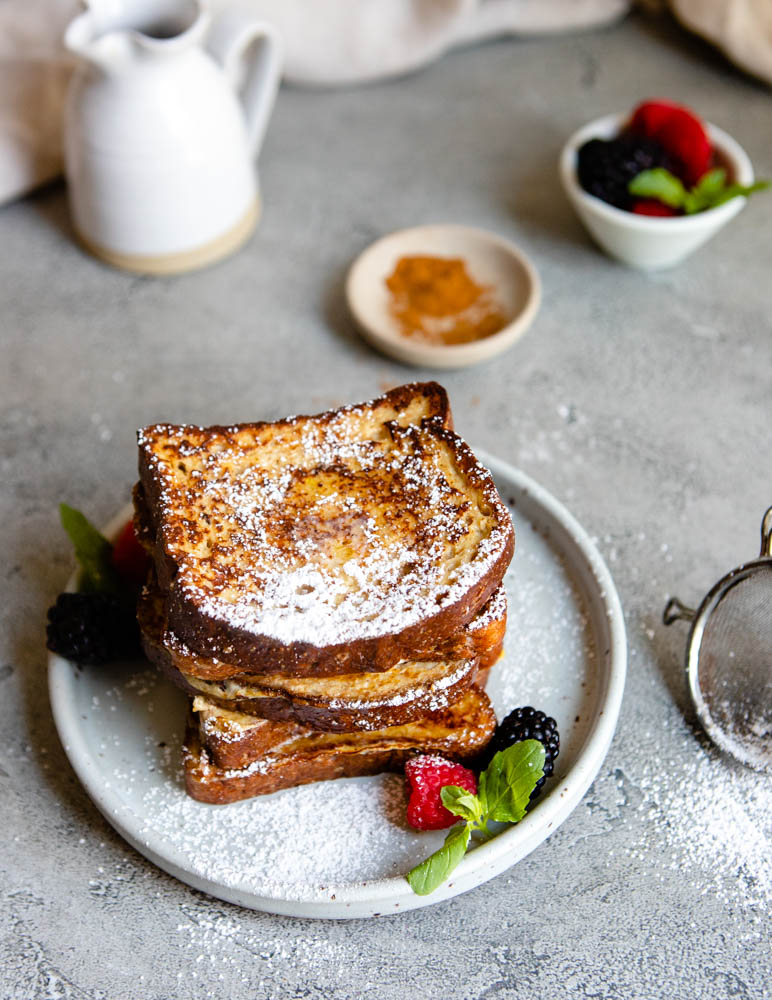 stacked french toast sprinkled with powdered sugar on a round plate 