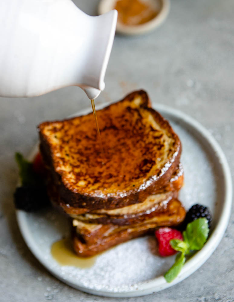 maple syrup being poured over a stack of French toast
