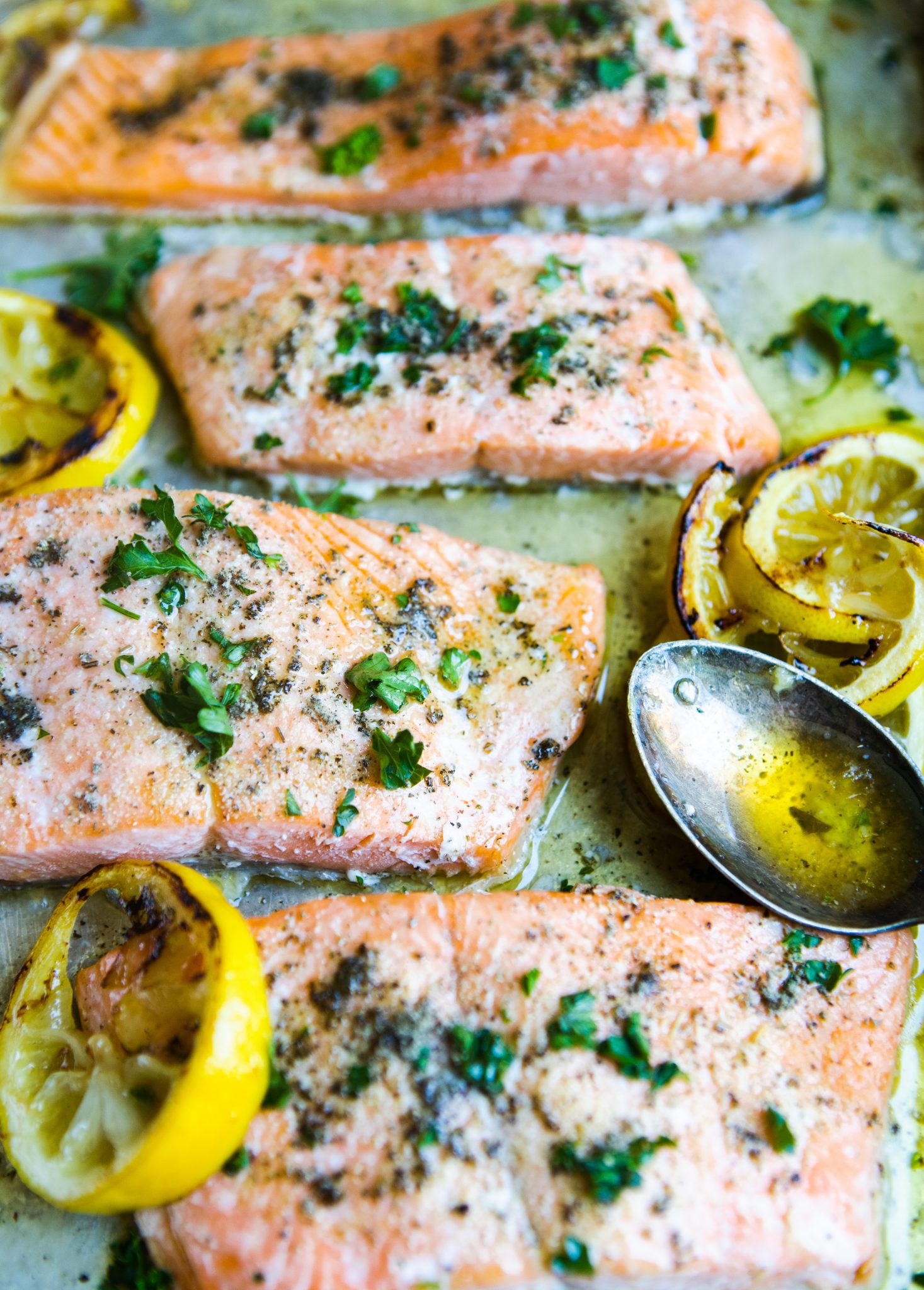 garlic butter salmon recipe cooked on a baking sheet with buttery lemon sauce drizzled with a spoon