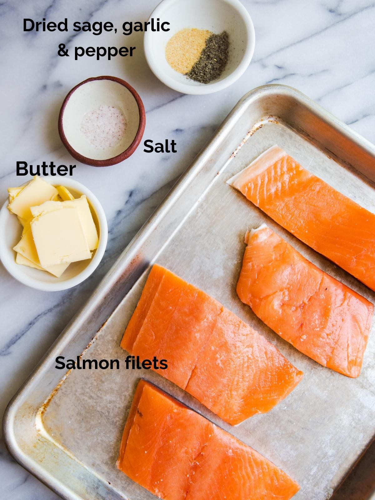 raw salmon filets on a baking sheet next to butter slices, dried sage and garlic and salt and pepper