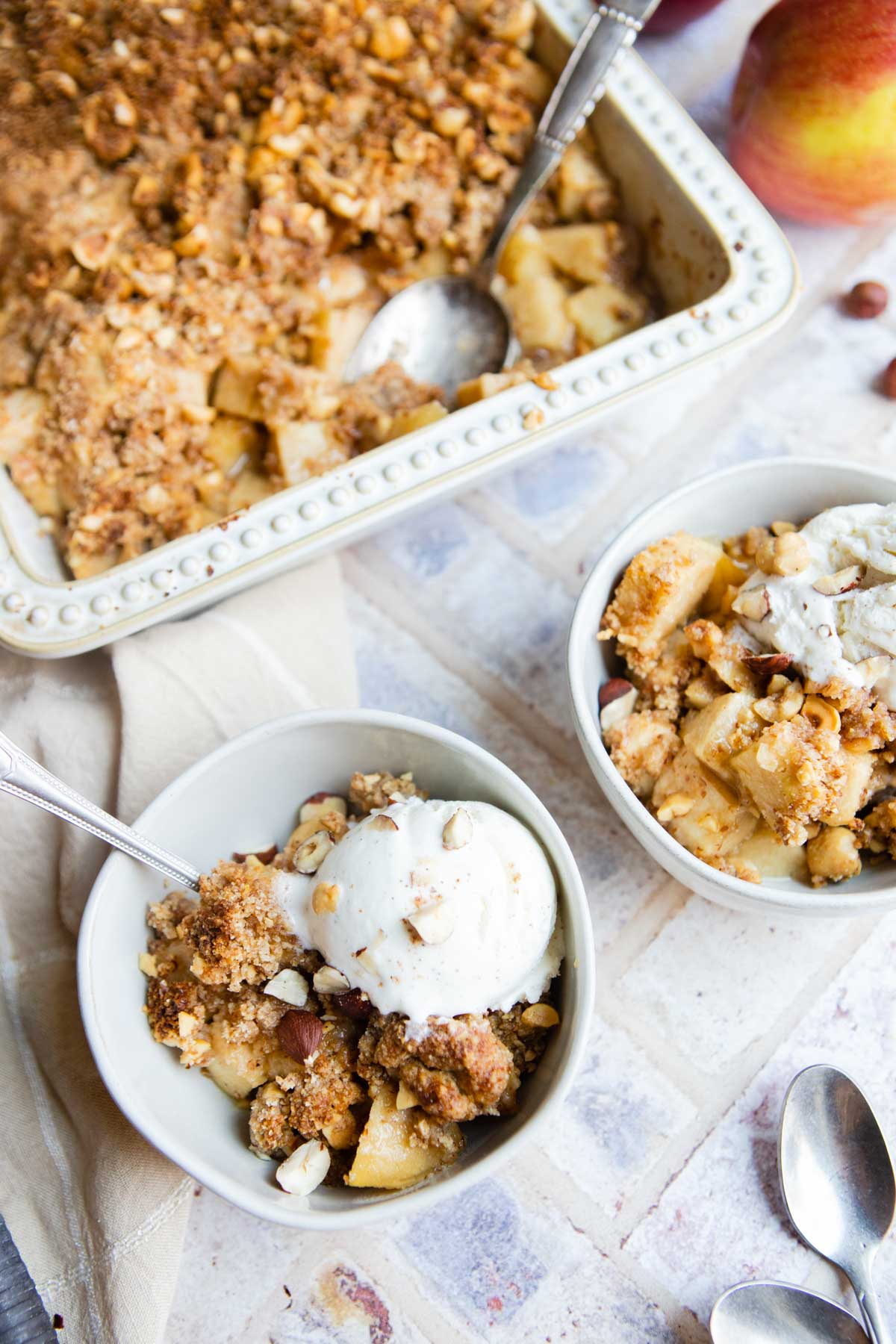 healthy apple crumble dessert baked in a white casserole dish scooped into 2 bowls with vanilla ice cream on top