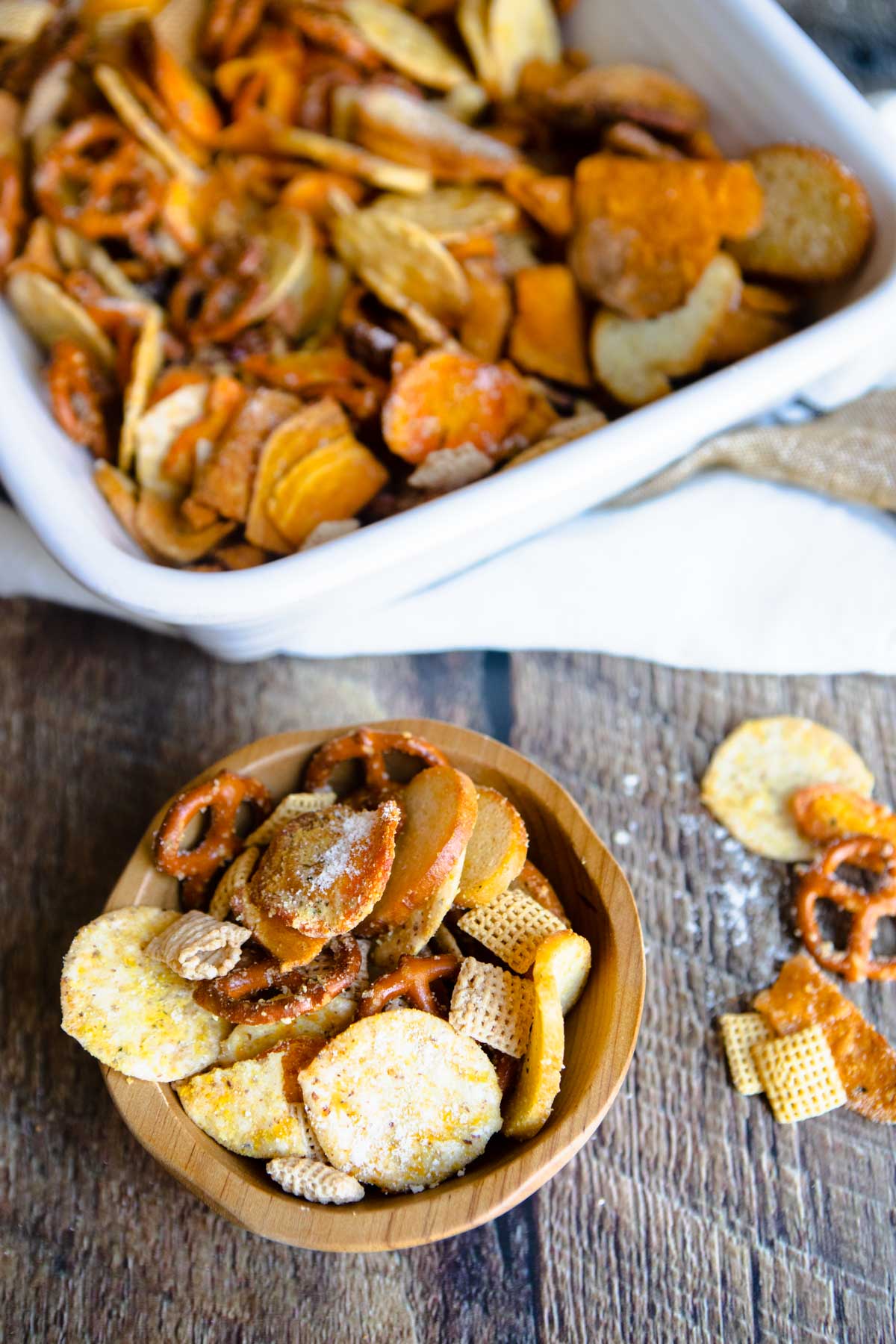 small wooden bowl holding a scoop of bold chex mix set on a wood table