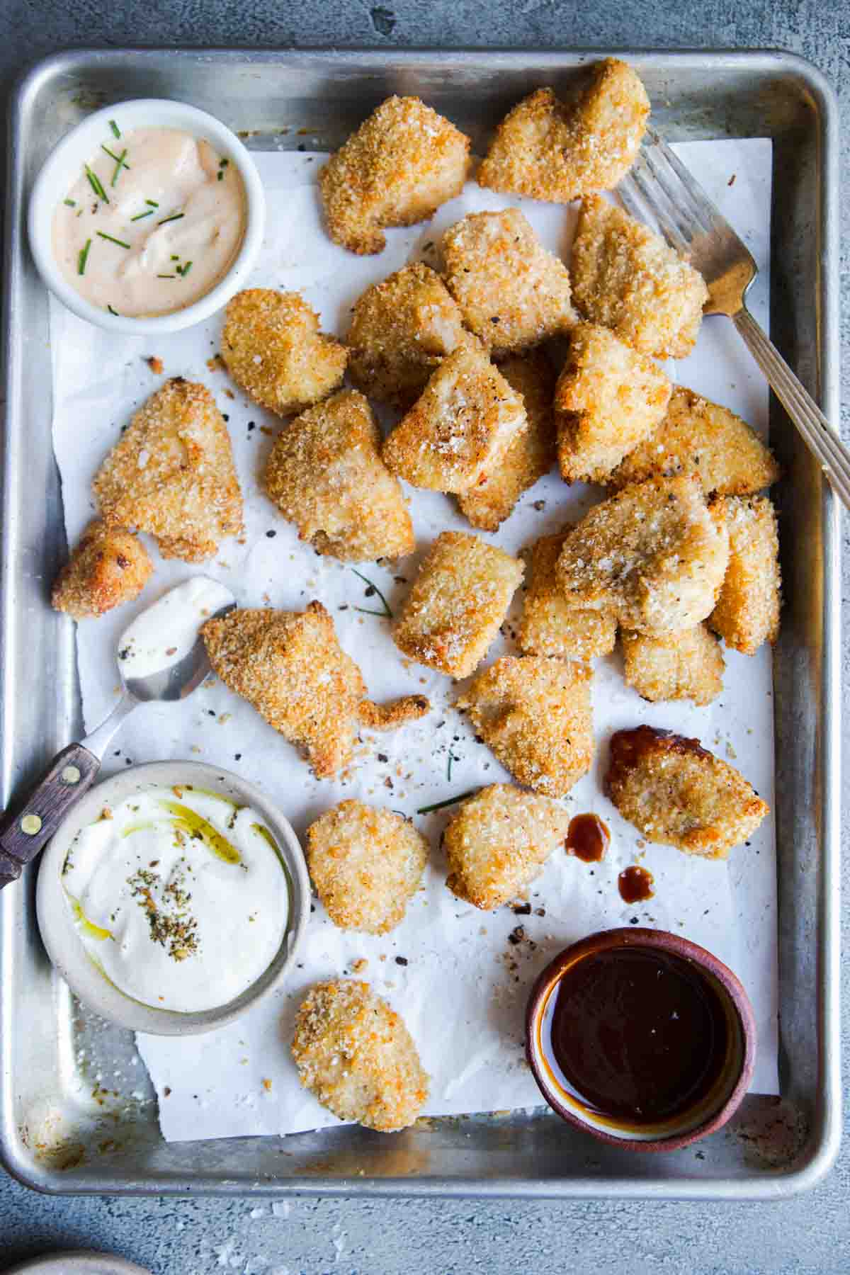 homemade chicken nuggets made in the air fryer on a rimmed baking sheet with dipping sauces 