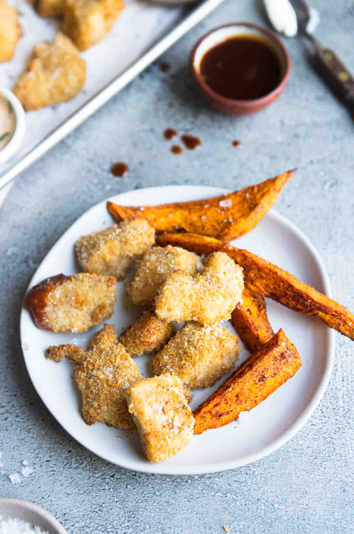 sweet potato fries and homemade chicken nuggets made in the air fryer on a round white plate 