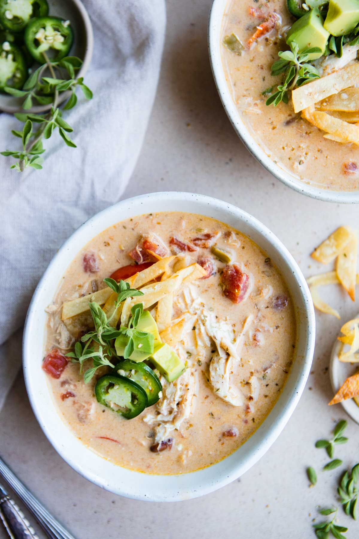 2 white bowls filled with creamy Mexican style chicken soup and garnished with jalapeno and avocado 