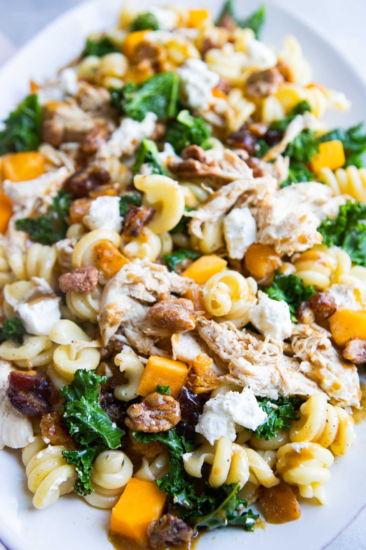 pasta and kale salad with shredded chicken, butternut squash and goat cheese on a white platter
