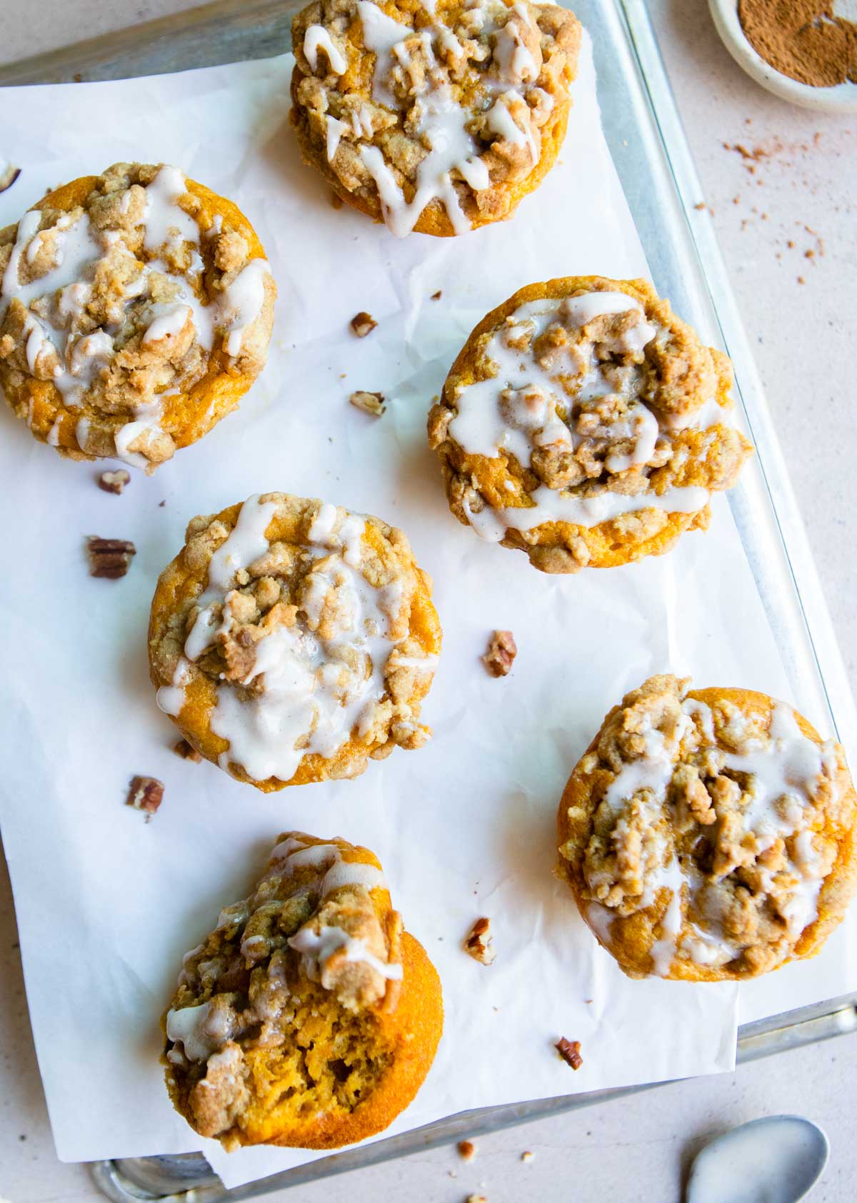 pumpkin banana muffins with a streusel topping and pumpkin spice glaze on a piece of parchment paper