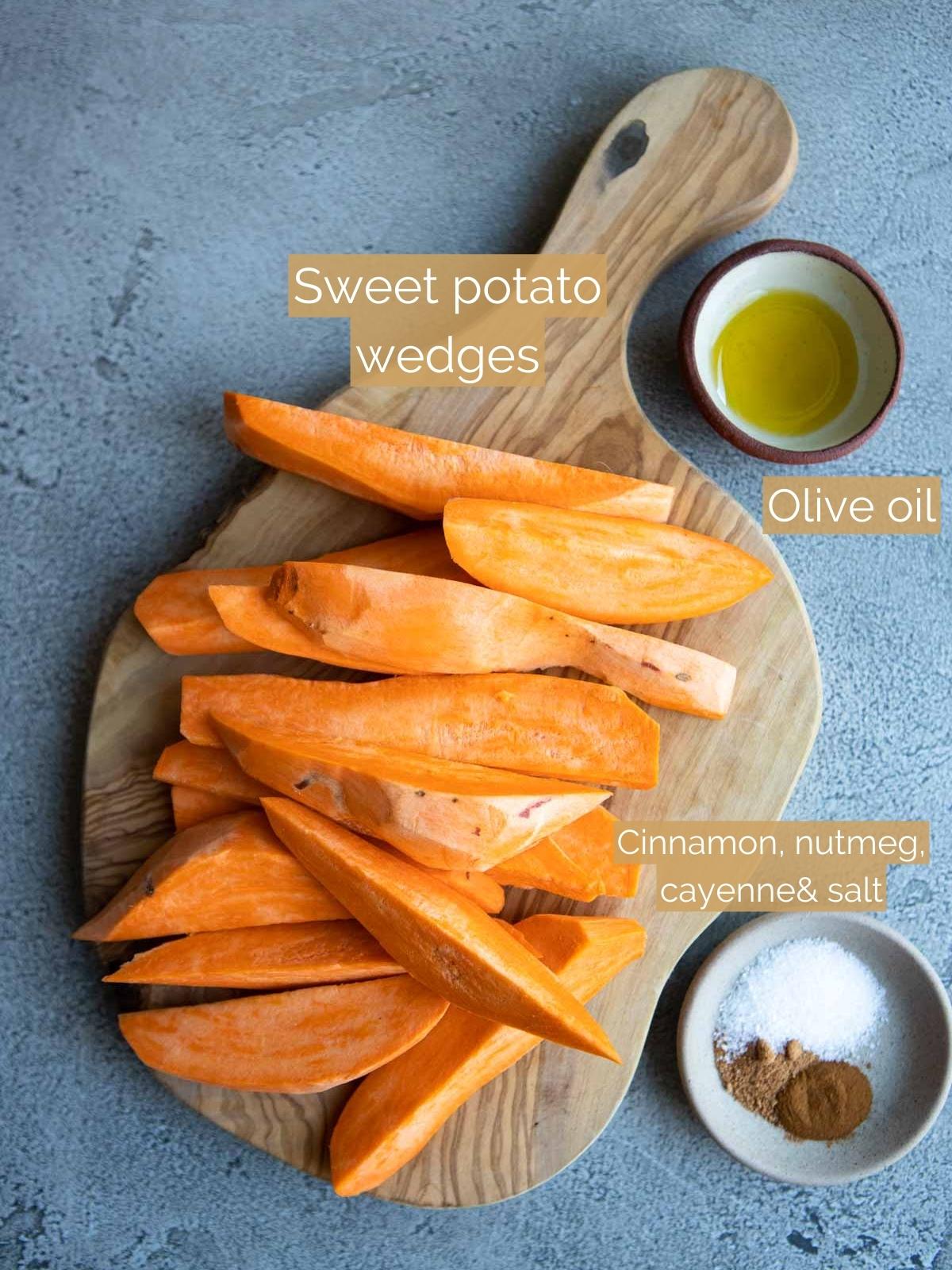 uncooked sweet potato wedges on a wood board net to a small bowl of olive oil and seasonings