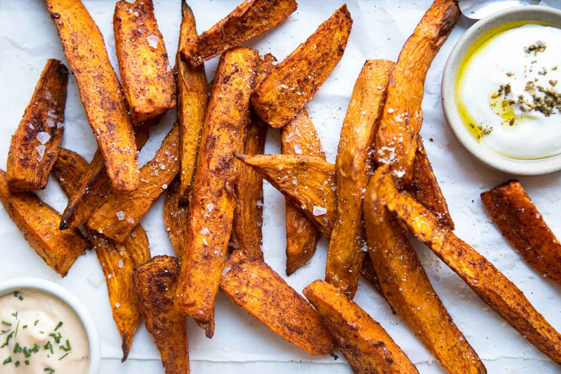 air fryer sweet potato wedges on a white piece of parchment paper sprinkled with parmesan cheese and salt