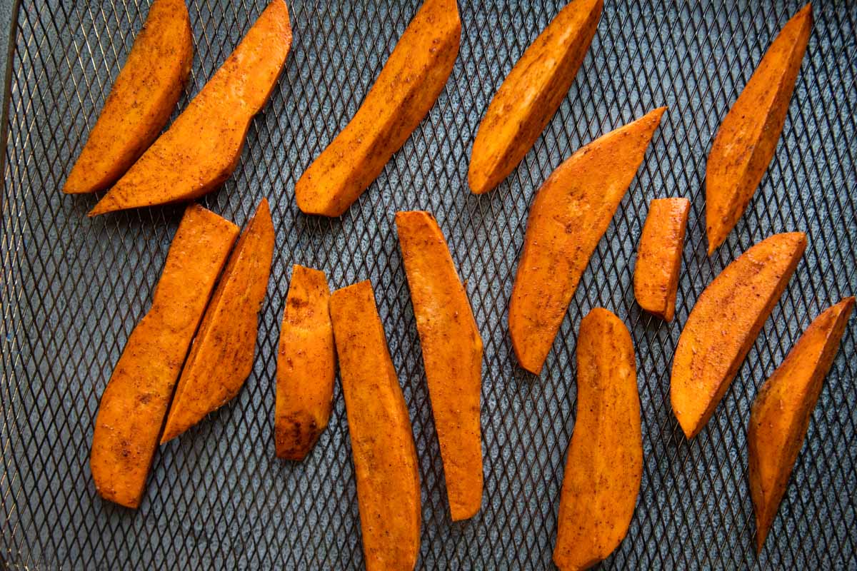 uncooked sweet potato wedges seasoned and placed on a air fryer tray